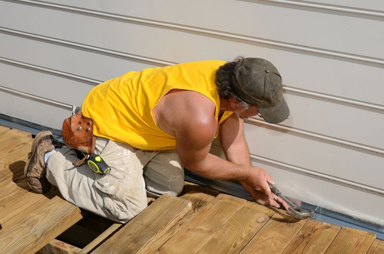 Burly contractor reattaching loose aluminum siding panel with hammer